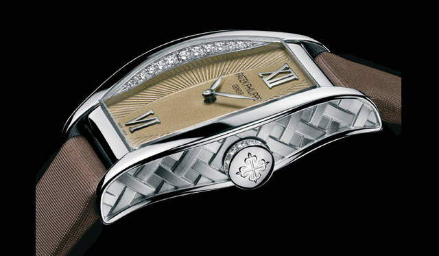 <strong>PATEK　PHILIPPE｜パテック フィリップ</strong>　ゴンドーロ4949。自社開発のクォーツ・ムーブメントを搭載したレディスタイプのトノー型ウォッチ。ダイヤモンドをベゼル内側にセッティングしたり、ケース側面に三つ編みのテキスタイルパターンを施すなど、ユニークなデザインワークが特長。文字盤の質感やカラーリングは、ブラウンのサテンベルトに合わせられる。