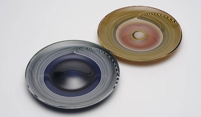 リビング・モティーフ│「fresco ～融けあう吹きガラスの色彩」展<br><b>hibiki（ヒビキ）</b>　吹きガラスの技法ならではの作品。材料が回転しながら吹き上げられていく過程は、あたかも音のようなモノが作品の中心から外側へ響いていくよう。その結果、音の痕跡のような表情をもった作品となった。プレート1万2600円