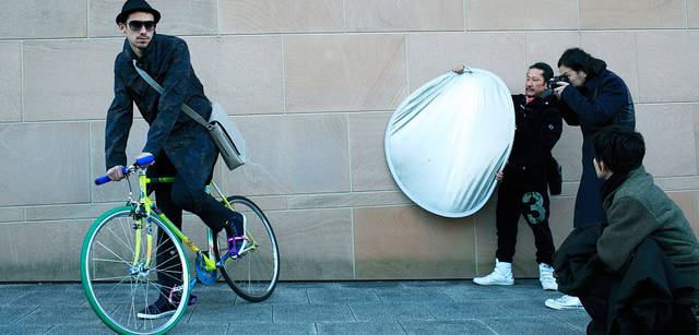 <strong>LOUIS VUITTON｜ルイ・ヴィトン</strong><br />いよいよ撮影スタート。凍えるような寒さのなか、シャッターをきる祐真さん。モデル｜タイガ・ラインのメッセンジャー・バッグ「ミロ」19万2150円、コート23万5200円、トラウザーズ 参考商品、サングラス5万1450円（すべて参考価格）、シューズ5万7750円（すべてルイ・ヴィトン／ルイ・ヴィトン カスタマーサービスセンター　Tel. 03-3478-2100）、ハットはモデル私物