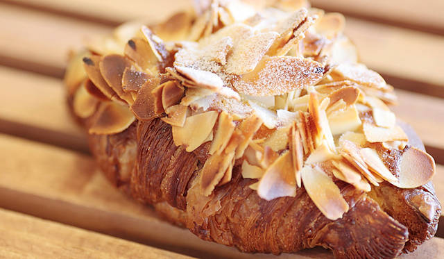 <b>Boulangerie Sudo｜ブーランジェリー スドウ</b>　クロワッサンの生地にラム酒入りのカスタードをはさみ、アーモンドクリーム、スライスアーモンドを載せて焼きあげた、贅たくな「クロワッサン ザマンド」 。焼き上がり予定時間 9:00　1個330円