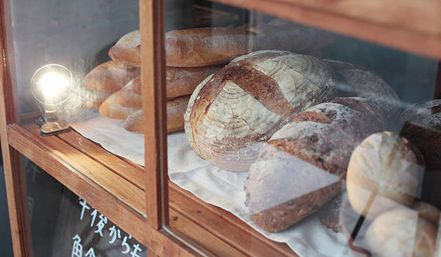 <b>AOSAN｜アオサン</b>　カンパーニュやバゲットが戸棚の中で出番を待っている。じつはこの戸棚は、奥田さんが自宅で使っていた食器棚。オープン時は、壁のペンキ塗りから内装や外装まで、電気とガス以外は自分たちで手がけたそうだ。