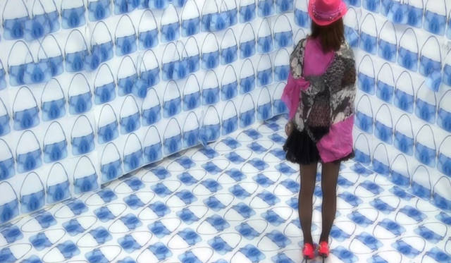 <strong>PRADA｜プラダ</strong>　『contrast』 立花 駿 作｜バンタンデザイン研究所大阪本校ヘアメイク学部</br>色を塗られた女性が、壁から天井まで部屋全体にヨーヨー バッグの紙の切り抜きが貼りつけられたシュルレアリスティックな部屋を見まわし、虚構と現実のコントラストを調べようとしている。