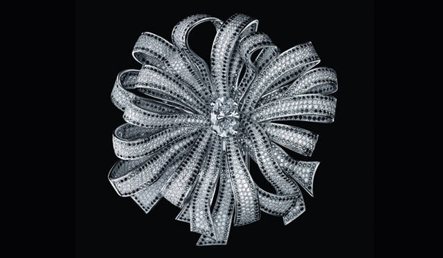 </br>優美で空気のように軽く、ネックや手首に官能的に巻きつくリボン。1932年、マドモアゼル シャネルは「ジュエリーが女性の指に柔らかなリボンのように結ばれるのが私の望み」と語り、これを“Bijoux de Diamants”（ダイヤモンド コレクション）のなかで見事に表現した。ダイヤモンドを散りばめた美しい輝きを放ちながら交錯するリボンは、このうえなく軽快かつフェミニン。ジュエリーの世界において革新的なこのコンセプトは、今日にいたるまで、シャネル ファイン ジュエリーの貴重なインスピレーション源なのだ。ブローチ[WG×ダイヤモンド×ブラックダイヤモンド]　3507万円　[参考価格] （シャネル）