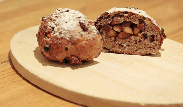 <strong>Loin montagne｜ロワンモンターニュ</strong>　卵、牛乳、バター不使用。北海道産全粒粉にクルミ、ラム酒漬けのカレンツ、愛媛産いよかんピール入りの生地で、素焼きしたマカデミアナッツを包み込んで焼きあげたパン「森の木の実」。焼きあがり予定時間9:00　1個170円