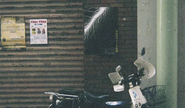 <strong>島田 明｜Life is Edit. #026</strong>　昭和の匂いを色濃く残す丸亀市内のいたるところに貼られた杉本作品のポスター。アナクロニズムの杉本さんに合わせて、わたしも使い捨てカメラでパチリ、してみました。