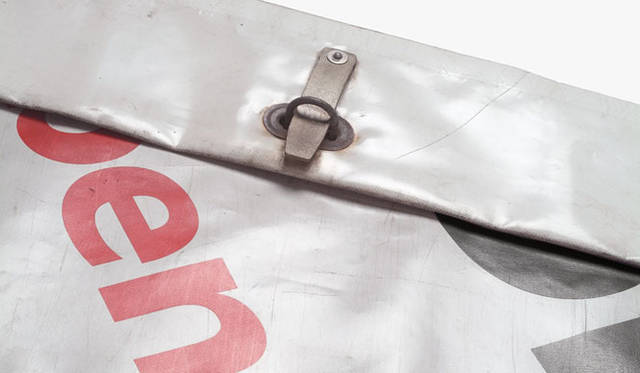 <strong>PASS THE BATON GALLERY</strong>　Recycled Truck Tarp / 年間使用量 300トン（トラック95KMの列に相当）<br>ヨーロッパのフリーウェイ上を縦横無尽に走る輸送トラックのタープ（幌）として平均5～8年を最初の役目として務めあげたあとは、産業廃棄物としてゴミになるのではなく、フライターグによってRecycle（リサイクル）ならぬ「Recontextualized（リコンテクスチャライズ）」されてバッグのメイン生地となり、トラック上ではなく、スピードも行き先もちがうひとの背中で2度目の役目を果たすこととなる。