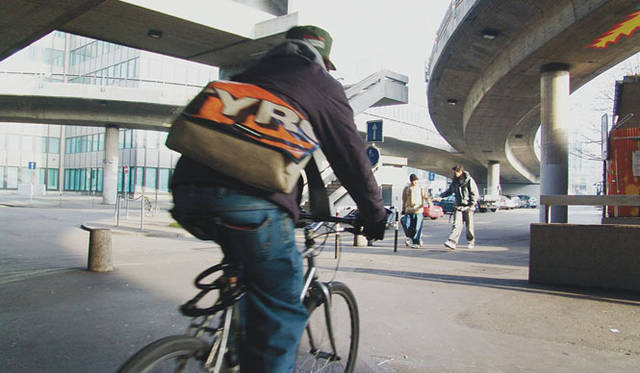 <strong>PASS THE BATON GALLERY</strong>　Hardbrücke<br>フライターグの心臓部、スイス・チューリッヒ中央駅の隣駅であるハルトブリュッケ。フライターグ創業から18年経過したいまでも、この橋を隔てた片側の「F-FACTORY」で幌を回収。洗浄したうえでカットし、梱包をおこなっている。もう片側には、使用済みのコンテナを積み上げてつくった高さ26mの旗艦店「F-SHOP ZURICH」がチューリッヒの街のランドマークとなってそびえたっている。