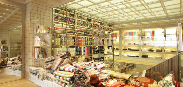 <strong>SUPER A MARKET｜スーパー エー マーケット</strong> 2階奥のコーナーからは、クリアな壁ごしに階段が見下ろせる。吹き抜けの壁面には、所狭しとカラフルな商品が。積み上げられているカラフルなラグは945円から、とお手頃な価格のものも。