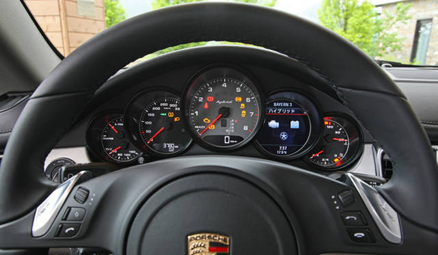 <strong>Porsche Panamera S hybrid｜ポルシェ パナメーラ S ハイブリッド</strong>　スピードメーターの右から2番目に配置されているハイブリッドと書かれた液晶は、現在の走行状態を指ししめしてる。この写真では、車輛の停止中のためモーターをあらわす右上のアイコン、タイヤ、エンジンをあらわす左上のアイコンのみが表示されているが、EV走行時はモーターからタイヤへ、ブレーキなど回生エネルギーが発生したさいはモーターへ、エンジン、モーター両方で走行するさいは双方からタイヤへ矢印が向けられる。