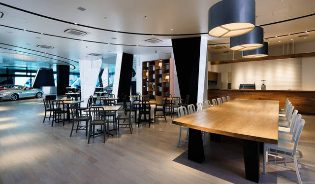 <strong>Mercedes-Benz｜メルセデス・ベンツ 「メルセデス・ベンツ コネクション」オープン</strong>　1階のカフェ「ダウンステアーズ コーヒー」。約5メートルのテーブルを配置し、そのテーブル中央から風力発電から生まれた電気が供給される。天井から吊らされているライトがメルセデスの象徴「スリーポインテッドスター」になっているのも印象的。チェアにはemeco社、111NAVY、天童木工製国産スツールが用いられる。