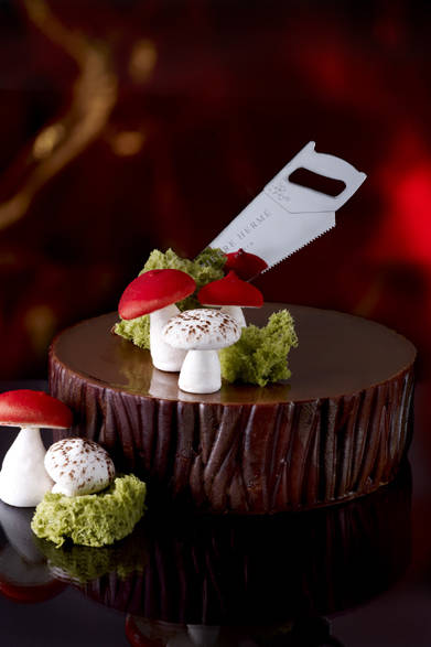 <strong>PIERRE HERMÉ PARIS｜ピエール・エルメ・パリ</strong><br />ノエル ア ラ カンパーニュ<br />丸太のようなケーキに大きなキノコ、プレキシグラス製のユーモラスなのこぎりが印象的なガトーは、子ども時代のクリスマスケーキの古き良き伝統のデコレーションをイメージしたもの。しっとりとしたアーモンド生地、かりかりのプラリネ、とろりとしたチョコレートガナッシュ、ぱりっとしたカカオ片に泡立つようなシャンティクリーム。さまざまな食感をもつ各層が呼応し合い、祝祭の気分を盛り上げる。<br /><br />価格｜8400円<br />予約期間｜12月20日（火）まで（予定）<br />販売期間｜12月21日（水）～25日（日）（予定）<br />展開店舗｜青山店限定