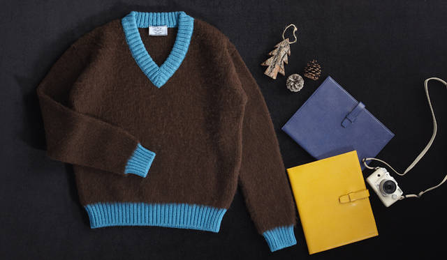 　豊かな風合いのあるニットは、落ち着いたブラウンに鮮やかなブルーの差し色がフレッシュなインパクトを与える。カラフルなiPadケースとコーディネイトして、ダークトーンでまとまりがちな冬のコーディネイトに軽やかなカラーをプラス。<br />メイドインペルーニット　7万9800円、iPadケース　各5万1450円　※各予定価格（すべてプラダ／プラダ ジャパンカスタマーリレーションズ　0120-559-914）