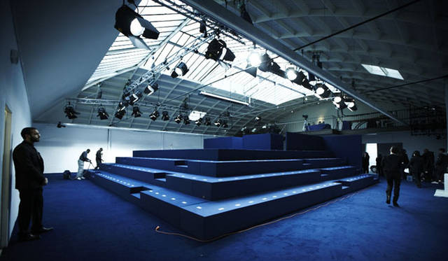 <strong>kolor｜カラー</strong>　ドアオープン直前。客席にシートナンバーを設置し、スタンバイ。ブルーと白の空間に客席4列＋スタンディングのピラミッド型客席は来場者を圧倒した