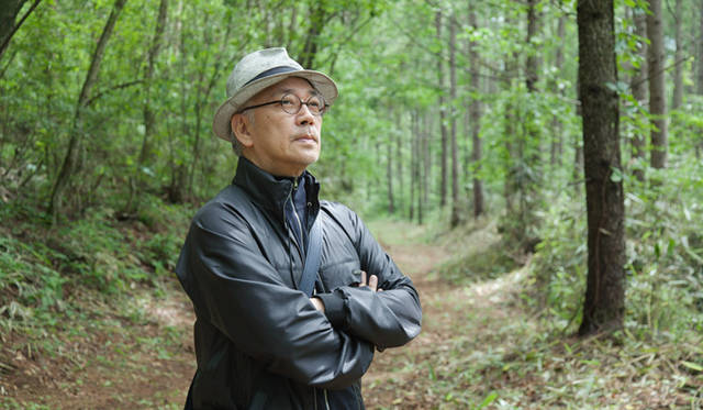 　間伐をして明るくなった「LOUIS VUITTON FOREST by more trees（ルイ・ヴィトンの森）」のなかに佇む、坂本龍一氏。「ここに来るのは今回で2度めですが、間伐されたところは本当に明るくなって。見た目にもきれいですよね。下にも草が生えて、全体的に美しい緑が広がった印象」