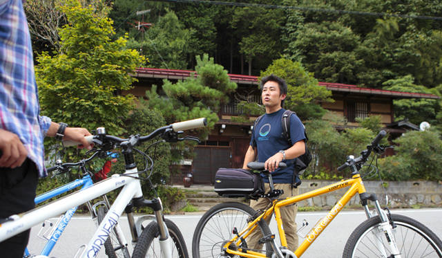 <strong>プロフェッショナルと巡る森～岐阜県の“ウェルネス・ツーリズム”</strong> 古民家を前にガイドをする「株式会社美ら地球（ちゅらぼし）」の代表取締役、山田 拓さん。「たくちゃん」の愛称で地元の人びとに親しまれている