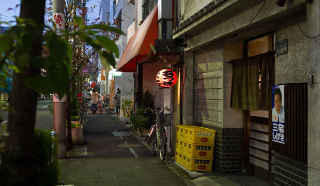 <strong>角田陽太｜東京浪漫酒場</strong>　三軒茶屋「久仁」　外観。薄暗いなかに小さな提灯が光る。手前の暖簾の店が久仁