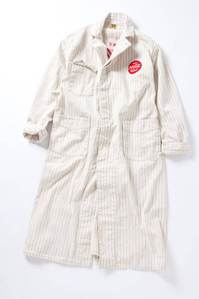 <strong>BEAMS｜ビームス</strong>　「COCA-COLA×HUMAN MADE×BEAMS」コレクション　戦前のワークウェアの作りを意識したショップコートに、同時期のロゴを配置。生地は「Cola-Cola」のセールスマンたちが着用していた歴史のあるオリジナルヘリンボーンを、1910年代の製法に限りなく近い形で再現。当時の刺繍の“ヨレ感”を表現するために、シンプルなラインの、1910年代の「Coca-Cola」ロゴをチョイス。刺繍はコンピュータ制御ではなく、ハンドルミシンで描くような歪（いびつ）なチェーン刺繍でおこなうため、箇所によって凹凸があり独特の風合いを表現している。ショップコートは元来作業時に着用するものだが、ステンカラーコートのような着こなしができるように、武骨なイメージを損なわない程度にサイジングを変えている。ショップコート5万1240円