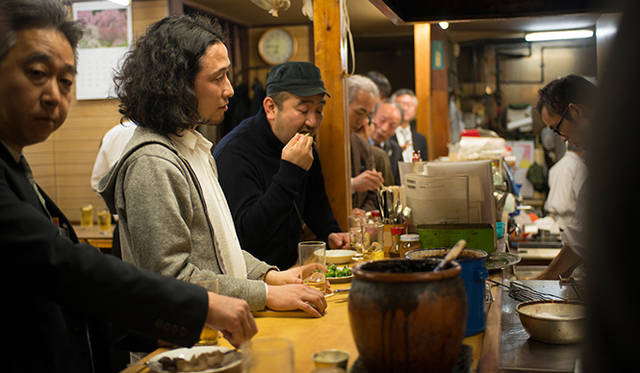 <strong>角田陽太｜東京浪漫酒場</strong>　恵比寿「縄のれん」　カウンターにびっしりのお客さんと角田陽太（手前から2人目）。立ち飲みなのに長居してしまうお店