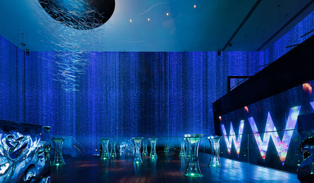 「フェイウルトララウンジ」のガラス面には18mにも及ぶ数万本のファイバー照明とテグスが天井から垂らされ、カーテン状に。そこにさまざまな光の風景が映し出される　Photograph courtesy of Nacasa & Partners Inc.