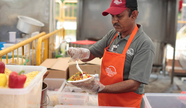 「バタタプーリ」に特製の香辛料とヨーグルトソースをかける、「India Gate Bhelpuri」のシェフ、グラブ・シン氏