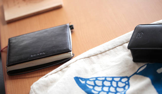 文庫本のカバーをかけた無印良品の「再生紙ノート・無地 A6」（左）と、リコーのコンパクトデジタルカメラ「GR」。中央のサブバッグは、旅先で使用するもの