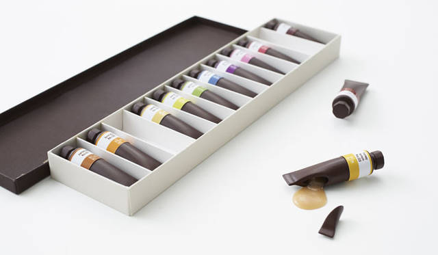 <strong>「chocolate-paint」for by｜n</strong><br />絵の具セットのようなチョコレート。チューブの中にさまざまな色の絵の具が入っているのと同様に、チョコレートの中にはそれぞれ異なるフレーバーのシロップが入っている。ラベルにはそれぞれのフレーバー名が書かれていて、食べるときには指を汚さないための包み紙の役目も果たしてくれる。子どものころにあたらしい絵の具の箱を開けたときに感じたワクワク感と、不意にプレゼントされたチョコレートの箱を開く瞬間のドキドキ感をリンクさせたデザイン。