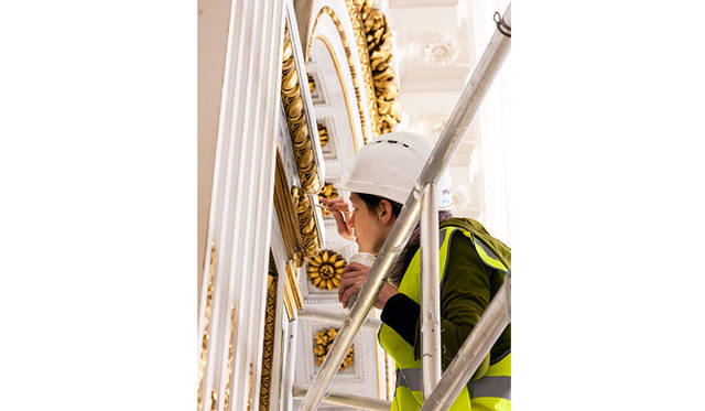 アトリエ・ゴアールの職人が、ル・ロビーの羽目板の細かい彫刻に金箔仕上げを施しているところ