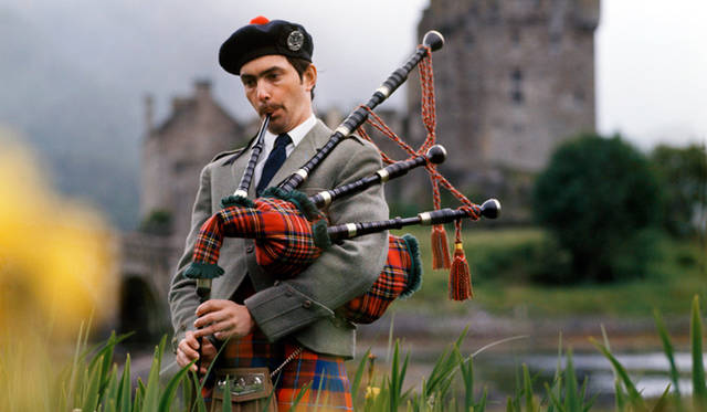 スコットランドの民族衣装　Man with bagpipes, Eilean Donan Castle, Highlands, Scotland, UK.  © VisitBritain / Britain on View