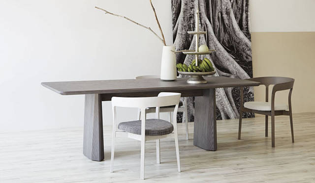 <strong>ダイニングテーブル「FIORD（フィヨルド）」</strong>　58万円（本体価格）<br />ダイニングテーブル、チェアともに藤森泰司氏デザイン。見る角度により表情を変えるテーブルは、“人が周りを自由に囲めるように”との想いからデザインされた。大胆な面構成、ダイナミックなフォルムの一方、天板縁には無垢材を配し重厚感を演出。特徴的な脚部は、木目の流れが途切れることなく仕上げられ、その彫刻的な存在感に、切り立った谷壁の間を水が流れるフィヨルドのような悠然とした様を重ねあわせている<br /><strong>チェア「RUNE（ルネ）」</strong>　手前・奥左／各16万円～（ビアンコオーク）、奥右／16万円～（グレーオーク／すべて本体価格）<br />ノルウェーのクラシカルなチェアに着想を得ながら、木の曲線でダイナミックに構成されたフルアームチェア。ゆとりあるサイズも特徴のひとつで、豊かな掛け心地とフィット感が味わえる