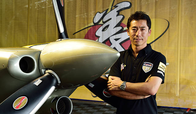 室屋義秀選手と愛機エッジ 540 V2。ゴールドはチームカラー。機体上部には秒針をイメージしたマークが入る。「ゴールドを選んだ理由は日本→ジパング→黄金郷という連想からです」と室屋選手。愛用するのは「ブライトリング　クロノマット44 GMT」だ<br />Photographs by KOJI NAKANO / BREITLING JAPAN