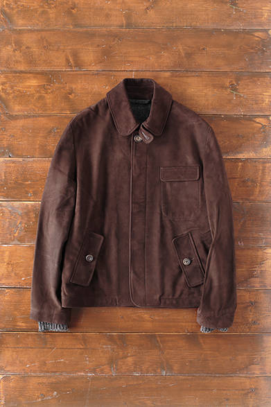 MENS｜胸元のフラップポケットと、チンストラップがアクセントとなった比翼仕立てのミニマルなデザインのブルゾン。滑らかで肌触りのいいヌバックカウレザーは、ハックニーのレザーワークショップにてオールハンドメイドで作られる。深みのあるダークブラウンが上質な雰囲気を醸す。また、カフはウエールズのニットメーカーによるラムウール、ライニングのファブリックはウエストヨークシャーの1980年代初頭設立の現存する唯一の自家完成形工場でつくられる。「british cowhide leather bz」26万8000円（S.E.H. ケリー）<br />※税抜価格
