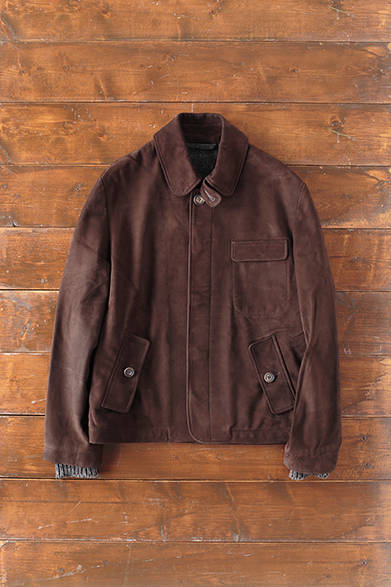 MENS｜胸元のフラップポケットと、チンストラップがアクセントとなった比翼仕立てのミニマルなデザインのブルゾン。滑らかで肌触りのいいヌバックカウレザーは、ハックニーのレザーワークショップにてオールハンドメイドで作られる。深みのあるダークブラウンが上質な雰囲気を醸す。また、カフはウエールズのニットメーカーによるラムウール、ライニングのファブリックはウエストヨークシャーの1980年代初頭設立の現存する唯一の自家完成形工場でつくられる。「british cowhide leather bz」26万8000円（S.E.H. ケリー）<br />※税抜価格