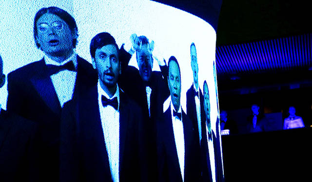 「Split Chorale for Viljo Revell」<br />だが、中央の柱に映し出される映像を見る自分たちを、合唱団が2階からのぞき込む形で配置されているため、だれが演じる側でだれが客なのかが分からなくなってくる