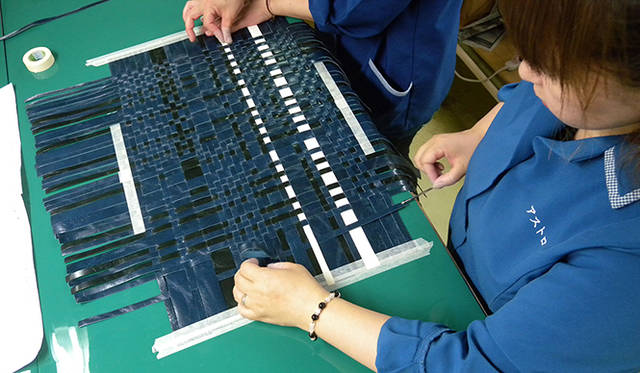 アストロ・テック社の女性スタッフがバッグのボディを手作業で編み込む風景 