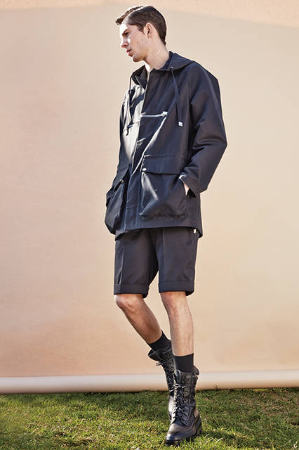 パターンワークとダーツで丸みのあるモードなショルダーラインを演出したコートは、スクエアなメタルパーツでよりエッジィな雰囲気に。ボトムスはショーツで軽やかさを出しつつも、ボリューミーなブーツでバランスの調和が図られている。<br><br>コート18万3600円、ショーツ4万8600円、ブーツ参考商品／バレンシアガ〈阪急メンズ大阪2階〉〈阪急メンズ東京2階〉