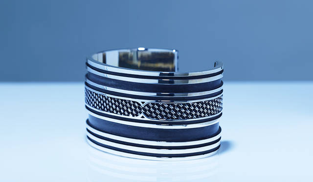 コンポジットシリーズならではの編み込み部分と、鏡面仕上げのライン、さらに黒く燻されたラインのコントラストが美しい、太めのバングル。存在感がありながらも、不思議と上品に身に着けることができる。<br /> <strong>「レイド バングル」</strong><br /> 価格25万円（税抜）