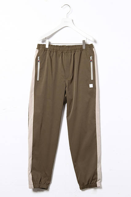 <strong>ウインドアップスーツ</strong><br /> コットンナイロンのストレッチ素材を使用した、ボリュームシルエットのスタンドカラージャケットと裾にゴムシャーリングを施したトラックパンツの組み合わせ。<br />  カラーは都会的なライトカーキとダークネイビー。パンツのサイドラインの柄はテニスプレーヤーであるBjon Borg（ビヨン・ボルグ）のシグネチャーモデルに採用されていたリブの柄にインスパイアされている。<br />  ウインドアップジャケット｜2万8000円（税別）<br />  ウインドアップパンツ｜1万8000円（税別）<br />