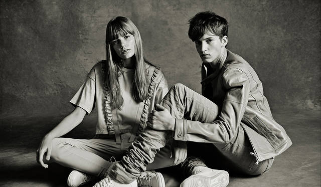 「休憩中の土木作業員のようなポージングですね。メンズは同系色でまとめた、ブランドアイコンのエクストラロングデニムにライダースジャケット。足元は編み上げブーツでもいいけれど、軽快なモダンさを出すためにハイカットスニーカーを合わせました。ウィメンズは、Tシャツ×デニムとこちらもワーキングクラスなカジュアルスタイルですが、ラッフルディテールが女性らしいアクセントになっています」（左）カットソー2万9000円、デニムパンツ3万6000円、スニーカー5万2000円（すべてディーゼル ブラック ゴールド）（右）ライダースジャケット19万円、デニムパンツ5万6000円（ともにディーゼル ブラック ゴールド）その他スタイリスト私物