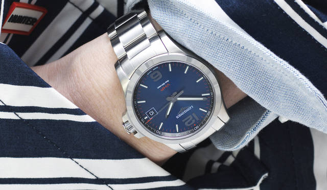 スーツ 31万4000円、シャツ 4万円、タイ 2万3000円（以上トム ブラウン）、フードパーカ 4万6000円（ハンター）、トートバッグ 3万5000円（ハンティング・ワールド）、その他スタイリスト私物<br><br><strong>コンクエスト V.H.P.</strong><br> Ref.｜L3.716.4.96.6<br> ムーブメント｜高精度クオーツ（Cal.L288.2）<br> 精度｜年差±5秒<br> 機能｜長寿命バッテリー、パーペチュアルカレンダー、スマートクラウン（※時差修正時、リューズを勢い良く回すと、針を一時間分スムーズに送ることができる）<br> ケース及びブレスレット素材｜SS<br> ケース径｜41mm<br> 防水｜5気圧<br> 価格｜12万1000円(税別)<br>