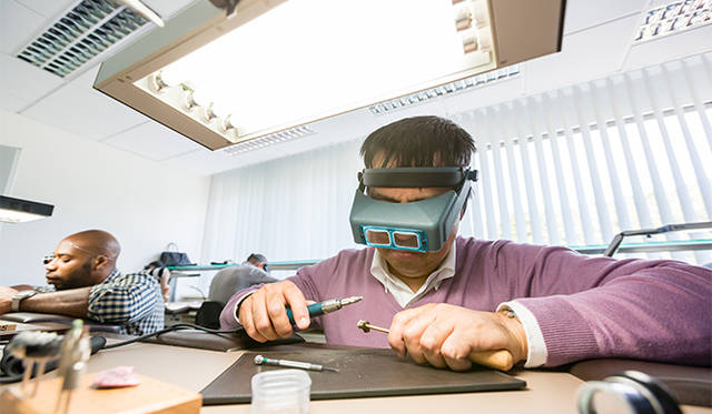 テンプ受けの面取り作業に挑戦中。左手で固定した部品に右手のグラインダーを当てていく。