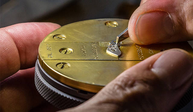 手作業で行われるテンプ受けへの彫刻。指と比べるとパーツの小ささがよくわかる。