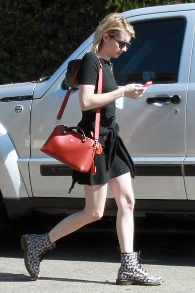 ハリウッドの街角に現れた女優のエマ・ロバーツ。ブラックのワンピースを着こなし、さりげない腰巻きのカーディガンがリラックス感を強調。赤いバッグと花柄のブーツがフェミニンなテイストを加えた。