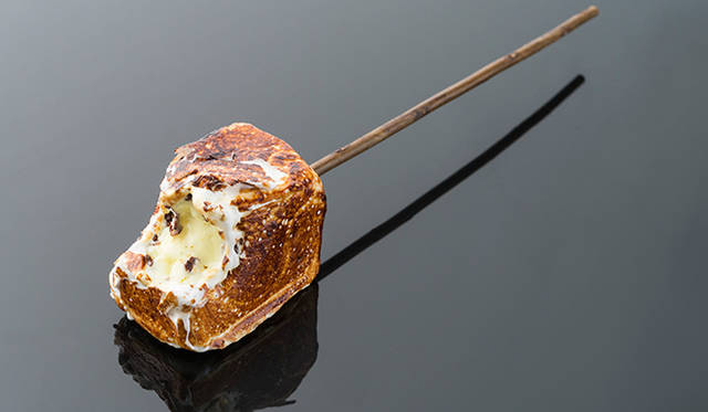 「フローズン スモア™」<br>アイスクリームをマシュマロで包み表面をバーナーで炙った、外はパリっとなかはとろとろ、さらになかのアイスクリームがひんやりの新食感スイーツ。キャンプファイヤーでマシュマロを炙る体験からインスピレーションを受けたメニューで、香ばしいキャラメルの香りとスモークで香りづけした手持ちの枝が、小さいころの思い出をよみがえらせる逸品。