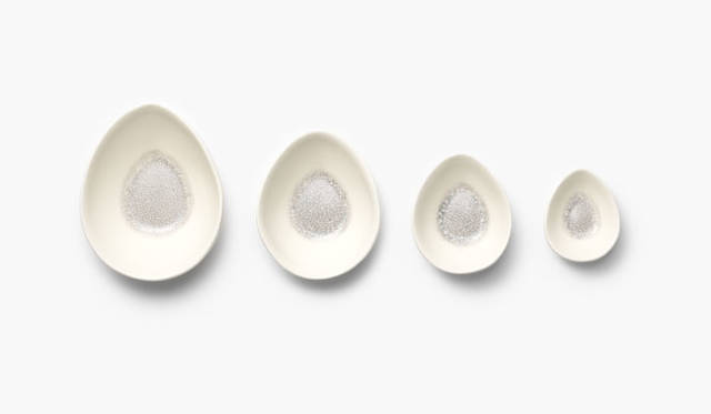 <strong>nendo｜ネンド</strong><br />「cs003（薩摩焼）」　薩摩焼は豊臣秀吉の時代にルーツがある鹿児島県の焼物で、白い素地に豪華な絵付けをほどこす白薩摩と、日常生活用に供される素朴で剛健な黒薩摩に大別される。この4点セットの器は白薩摩で、白い素地に釉薬を使ってタマゴを思わせる色と形に。器全面に「貫入」と呼ばれる、焼成時の素地と釉薬の収縮率の差によって発生させた意匠的なヒビ割れがあり、器の内側底部の貫入に顔料を入れ、その濃度を変えながら押し広げていくことで、白い素地から黒いグラデ―ションが生まれている。4つの器は重ねたときに口縁が段差なく収まる。Photographs by IWASAKI Hiroshi