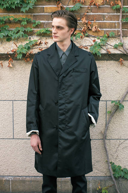 ナイロン素材のチェスターフィールドコートは、シングル仕立てで、前の合わせが深い独特なデザイン。ショルダーにはミリタリー感覚のループが付いていて、グレー色のコットンシャツと相まって、モダンマスキュリンな男性像をイメージさせる。 <br><br> コート24万4080円、デニム6万6960円、シャツ6万6960円［すべて予定価格］（プラダ／阪急メンズ大阪2階）
