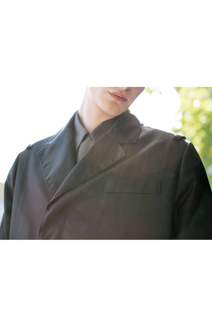 ナイロン素材のチェスターフィールドコートは、シングル仕立てで、前の合わせが深い独特なデザイン。ショルダーにはミリタリー感覚のループが付いていて、グレー色のコットンシャツと相まって、モダンマスキュリンな男性像をイメージさせる。 <br><br> コート24万4080円、デニム6万6960円、シャツ6万6960円［すべて予定価格］（プラダ／阪急メンズ大阪2階）