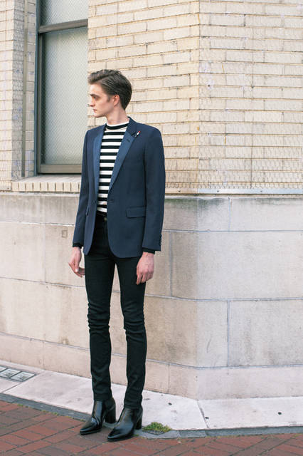 ネイビーのスモーキングジャケットにハイウエストのスキニーデニムを合わせたコーディネートは、エディ・スリマンらしい感性に満ちたもの。 ハイネックのインナーをタックインしたスタイリングのセンスも洒脱。ヒールブーツを合わせて統一された世界観そのものを着こなしたい。 <br><br> ジャケット31万9140円、パンツ7万2900円、ニット10万9620円、ブーツ18万3600円（サンローラン／阪急メンズ大阪2階、阪急メンズ東京2階）