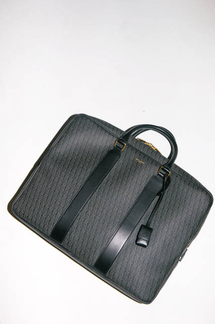 モノグラムが描かれたブリーフケースは、ファスナーやキーといった部分に使われたゴールドが艶やかさを加える。ハンドル部分と前後のパネル部分のレザー切り替えで、モードとラグジュアリーな感性をミックスさせたデザイン。 <br><br> バッグ［W36×H27×D9.5cm］15万6600円（サンローラン／阪急メンズ大阪2階、阪急メンズ東京2階）