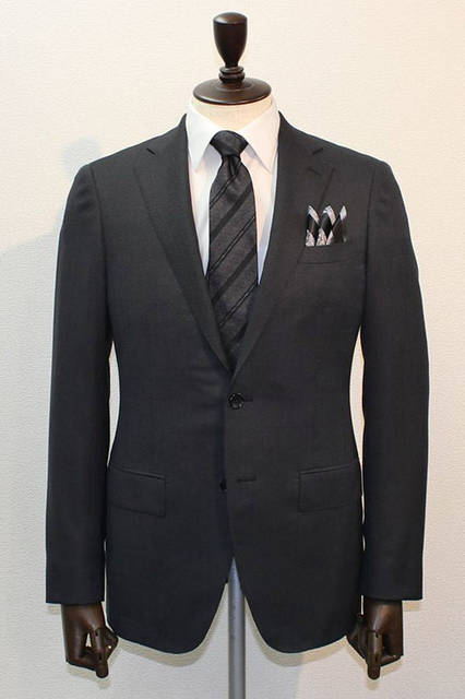 <strong>D'URBAN｜ダーバン</strong><br />2015-16年秋冬コレクション　今季打ち出しのアムンゼン柄無地調スーツは、横糸にシルクを使用し、ソフトなシャンブレー感に光沢がくわわった生地が特徴。無地調のダークグレースーツに白無地シャツ、ブラック×グレーのレジメンタイ、3ピークのチーフというコーディネート。スーツ10万6920円