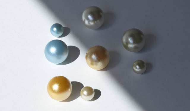 「tone pearl」Designed by AZUCHI　真珠の光沢が放つ繊細な色の変化はつねに人びとを魅了してきた。人類がその光沢を自らつくりたいと願い生まれたのが人工真珠だ。その光沢はもはや本物と見分けがつかないレベルにまでにいたっている。人工真珠の角度により変化する繊細な色を、別の要素からさらに変化させることができれば、本物すら届かない美に辿り着けるのではないかと考えた。今回、紫外線で発色する塗料を用いることにより、太陽の光と影であらたな色が生まれる人工真珠の開発を試みた